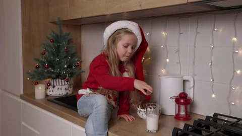 Funny kid in red santa's hat eating christmas cookies with milk on the Stock Footage 166466388