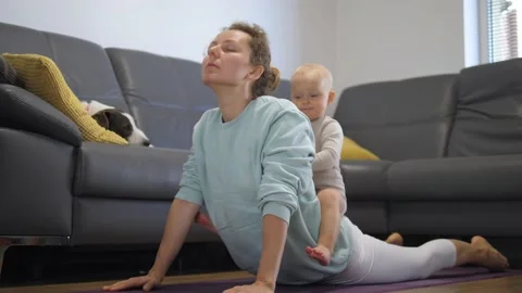 Funny kid sitting on mom's back during her home yoga class. In-house physical Stock Footage 144901659