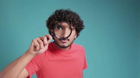 Funny latin hispanic man looking through magnifying glass, searching or Stock Footage 239361457