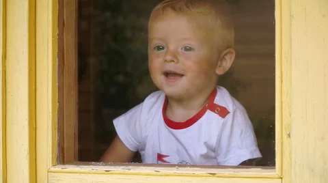 Funny little boy of 1,5 years idoors looks out the window and rejoices Stock Footage 65774853