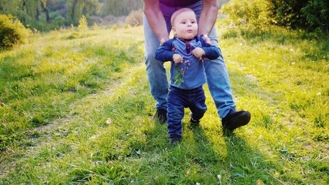 Funny little boy learns to walk. His hands are supported by his father. The boy Stock Footage 75406300