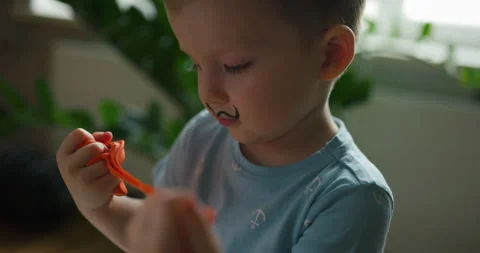 Funny little boy with painted mustache playing with orange modeling clay Stock Footage 334669152