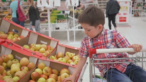 Funny little boy picking apple from the box sitting in the trolley, during Stock Footage 90250480