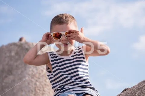 Funny little boy in sunglasses and sailor vest sitting on concrete breakwater Stock Photos
