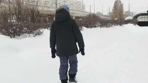 Funny little boy in winter clothes walks during a snowfall. Outdoors Stock Footage 150520368