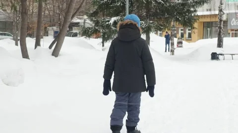 Funny little boy in winter clothes walks during a snowfall. Outdoors Stock Footage 150520405