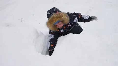 A funny little boy in a winter down jacket digs a snow hole with a toy shovel Stock Footage 145243794