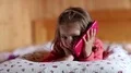 Funny little girl with big red smartphone lies on the bed HD Footage
