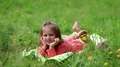 Funny little girl in glasses lies on the green grass and looks at the camera HD Footage