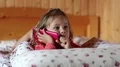 Funny little girl with red smartphone lies on the bed and picks his nose HD Footage