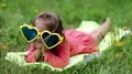 Funny little girl in sunglasses in shape of hearts lies on grass and grimaces HD Footage