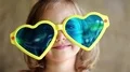 Funny little girl in yellow and blue glasses looks at camera and shows tongue HD Footage