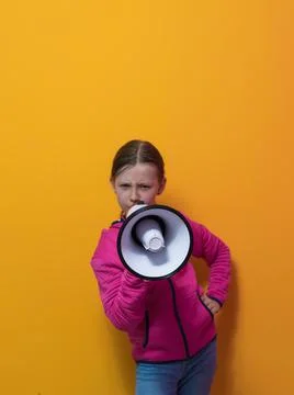 Funny little kid girl Screaming in megaphone over the yellow background in Stock Photos