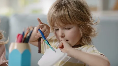 Funny little kid playing while crafting something. Cute boy cutting paper with Stock-Footage 128049845