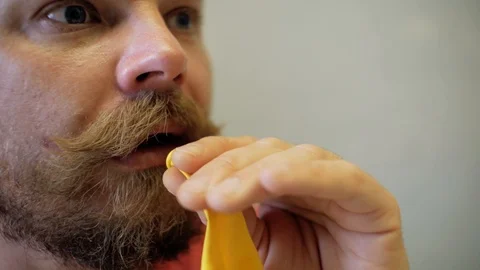 Funny man with a beard and mustache inflates a yellow balloon with his mouth Stock Footage 104843117