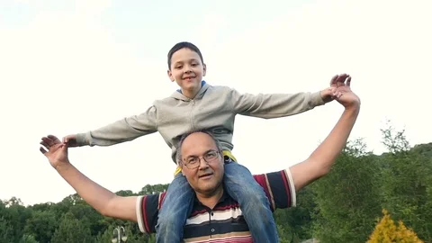 Funny man with a boy on his neck tilting left and right in park. Slow motion. Stock-Footage 70951322