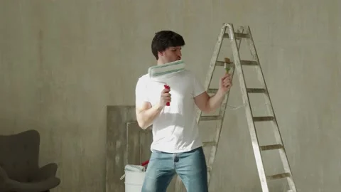 Funny man with a brush and roller dances, moves and sings during the renovation 스톡 동영상 153837835