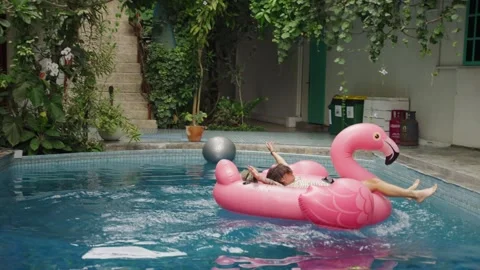 Funny man does a flip on an inflatable pink flamingo in the pool on vacation Video stock 267921764