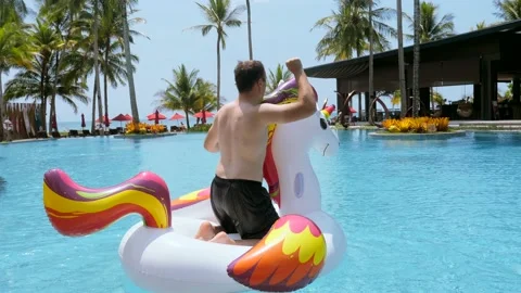 Funny man having fun, dancing on floating inflatable unicorn, tropical vacation Video stock 180874880