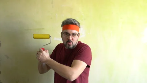 Funny man holds a roller for rolling wallpaper and plays with it 4K Video stock 126125929