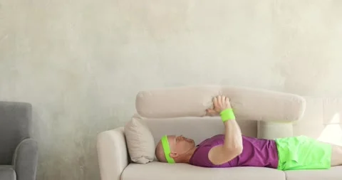 Funny man is making exercises pulling pillow lying on sofa, fitness humor. Stock Footage 131232826