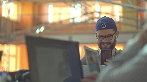 Funny man in modern shared working space smiling using smartphone lrrl. surfing Stock Footage 136374584