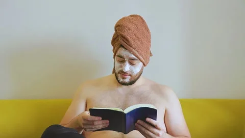Funny man reading book sitting on sofa relaxing at home, Stock Footage 166164977