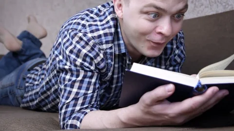 Funny man reading book while lying on couch at home. Knowledge and learning Stock Footage 129663362