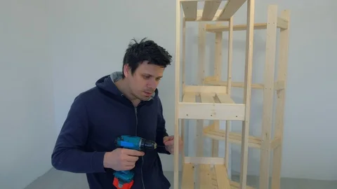 Funny man screws boards using electric screwdriver collecting rack furniture. Stock Footage 129592778