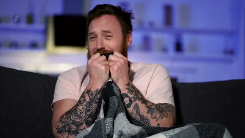 Funny man sitting on the sofa, crying and watching sad moovie. Slowmotion. Video stock 122200485