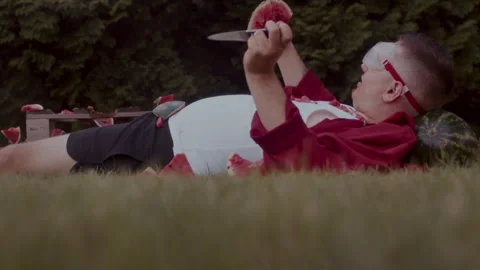 Funny man slicing watermelon while laying on the ground Video stock 258303747