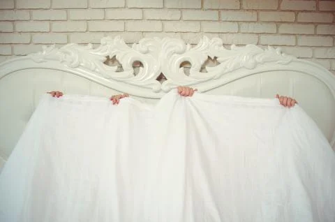 A funny married couple, lying in bed and hiding under a white blanket, only a Stock Photos