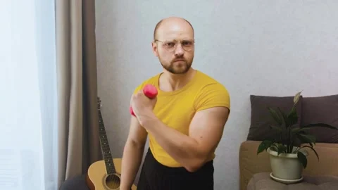 Funny nerd with glasses menacingly and does biceps exercises with pink dumbbells Stock-Footage 243755372