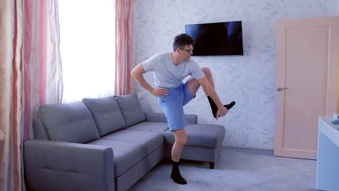 Funny nerd man is doing stretching exercise for leg, trying to lift his leg up Stock Footage 114353064