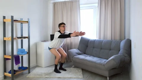 Funny nerd man in glasses and shorts doing complex of fitness exercises at home. Stock Footage 154160187