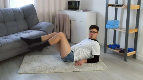 Funny nerd man in glasses doing fitness exercise for abs lying on floor at home. Video stock 153258978
