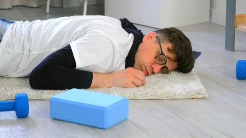 Funny nerd man in glasses is falling on carpet and sleeping on floor at home. Stock Footage 153261802