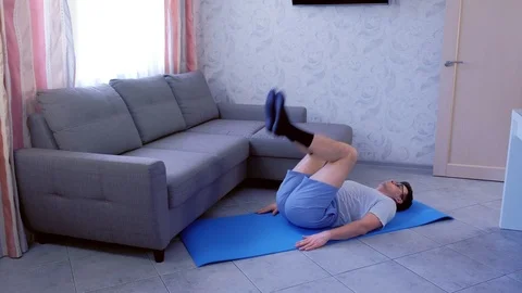 Funny nerd man is lifting legs lying on mat at home. Sport humor concept. Stock Footage 114434686