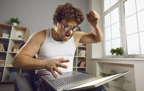 Funny nerdy man having problem with his laptop, shouting and threatening to Stock Photos