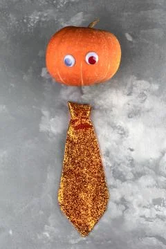 Funny orange pumpkin with eyes and shiny tie on grey cement background. Autum Stock Photos