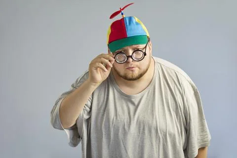 Funny overweight man in propeller cap adjusting glasses, playful comic pose Stock Photos