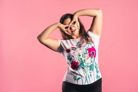 Funny plus size model making finger glasses, cheerful fat woman on pink backg Photos