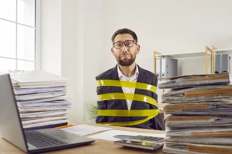 Funny, sad work slave, restrained with adhesive tape, sitting at office desk Stock Photos