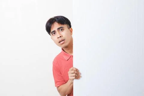 Funny scary face expression of a young man peeking from behind a blank boar.. Stock Photos