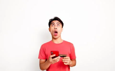 Funny shocked customer looking up while holding smartphone and credit card .. Stock Photos