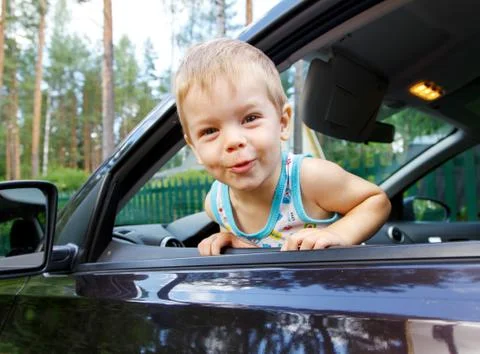 Funny small kid looking from open car window Stock Photos