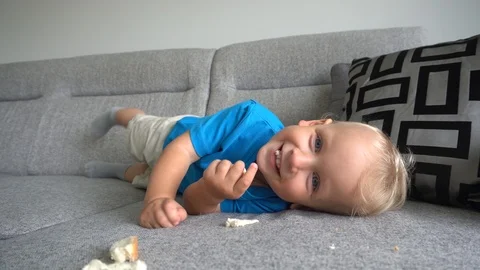 Funny smiling boy lying on sofa and eating white bread. Smooth camera motion Stock Footage 124362504