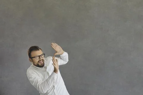 Funny smiling scared man closing face with hand standing on grey background Stock Photos
