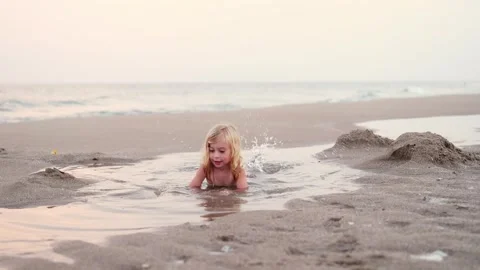 Funny smiling three years old girl lying in puddle on sandy beach , laughing Stock-Footage 247220228