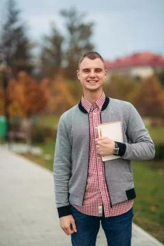 Funny student with notebook. Guy stand in park and smile Stock Photos
